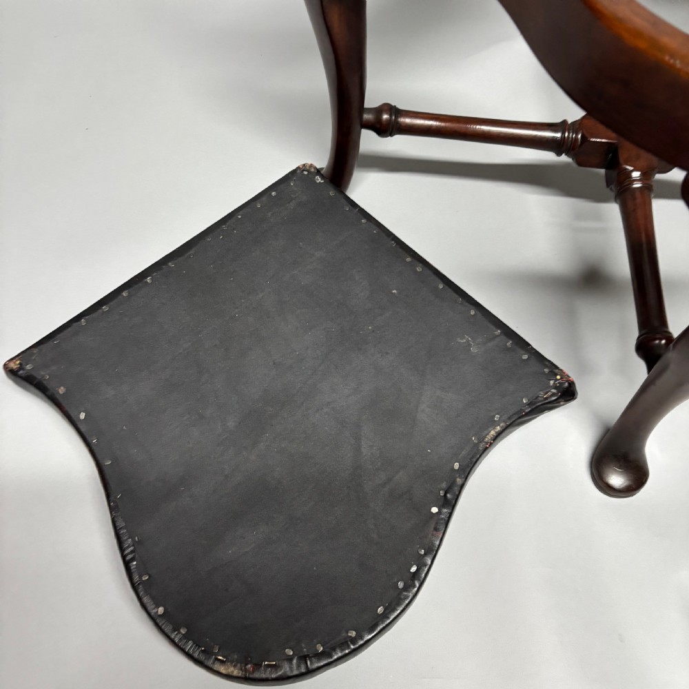 An 18th-century George III dark mahogany corner chair featuring a curved top rail, twin shaped splats, a dark leather seat, turned stretchers, and a front cabriole leg carved with a shell motif. View XII