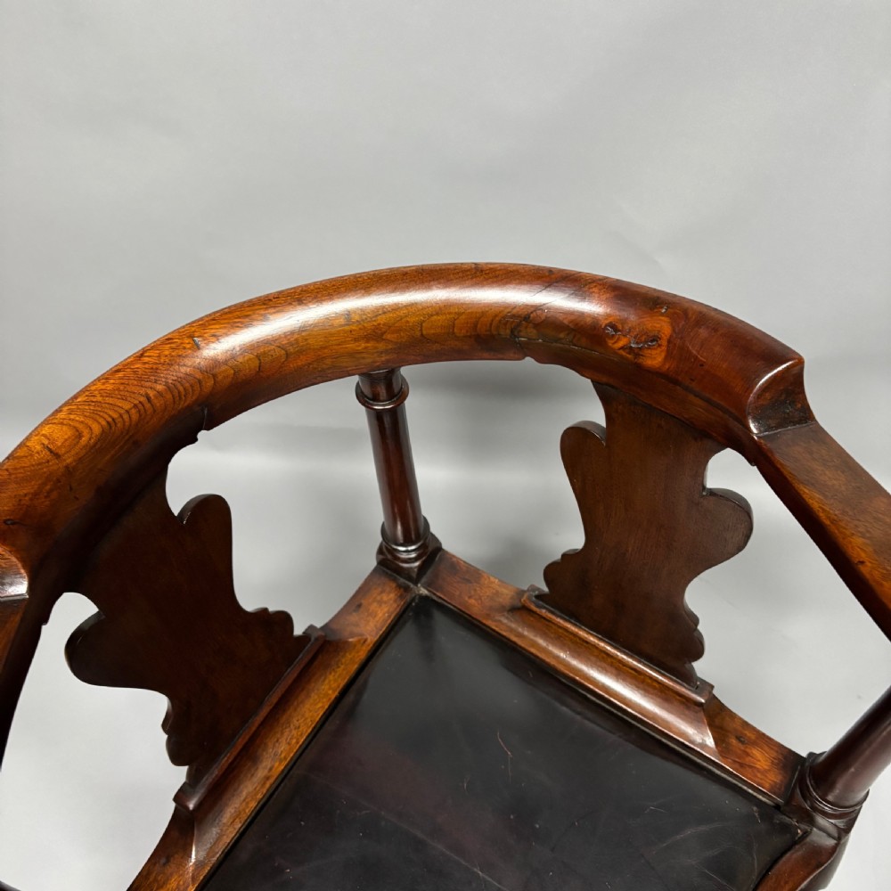 An 18th-century George III dark mahogany corner chair featuring a curved top rail, twin shaped splats, a dark leather seat, turned stretchers, and a front cabriole leg carved with a shell motif. View XXIII