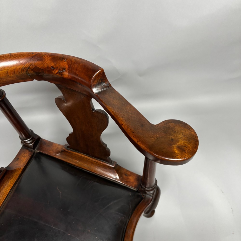 An 18th-century George III dark mahogany corner chair featuring a curved top rail, twin shaped splats, a dark leather seat, turned stretchers, and a front cabriole leg carved with a shell motif. View XXIV