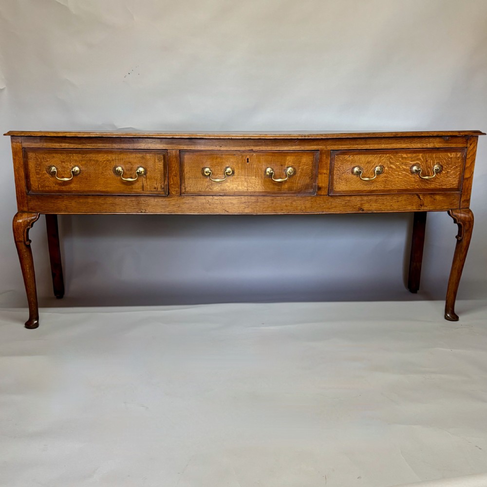 A George III period oak dresser base featuring three drawers with brass swan-neck handles and front cabriole legs.