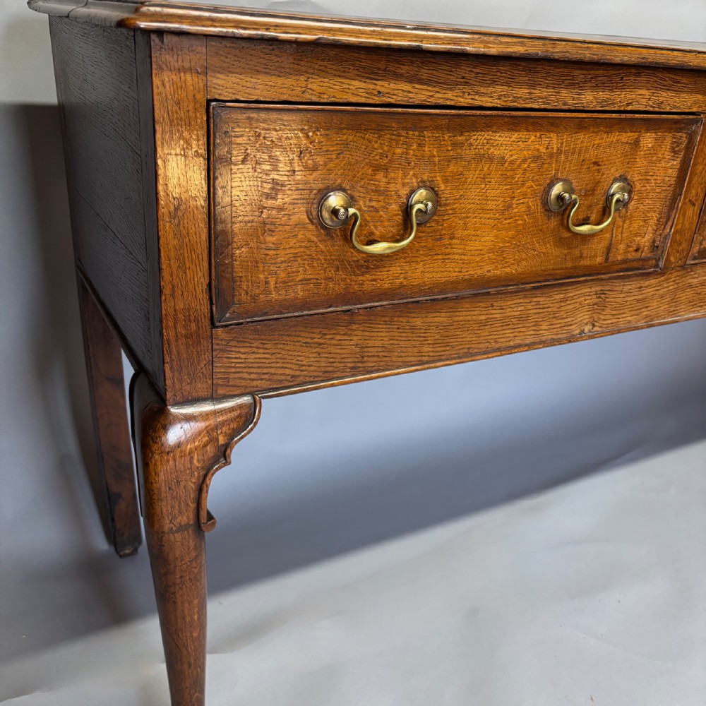 A George III period oak dresser base featuring three drawers with brass swan-neck handles and front cabriole legs. View VI