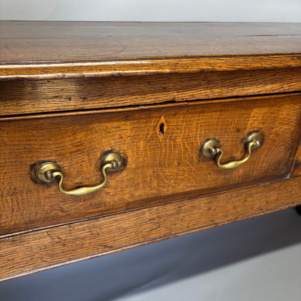 A George III period oak dresser base featuring three drawers with brass swan-neck handles and front cabriole legs. View VII