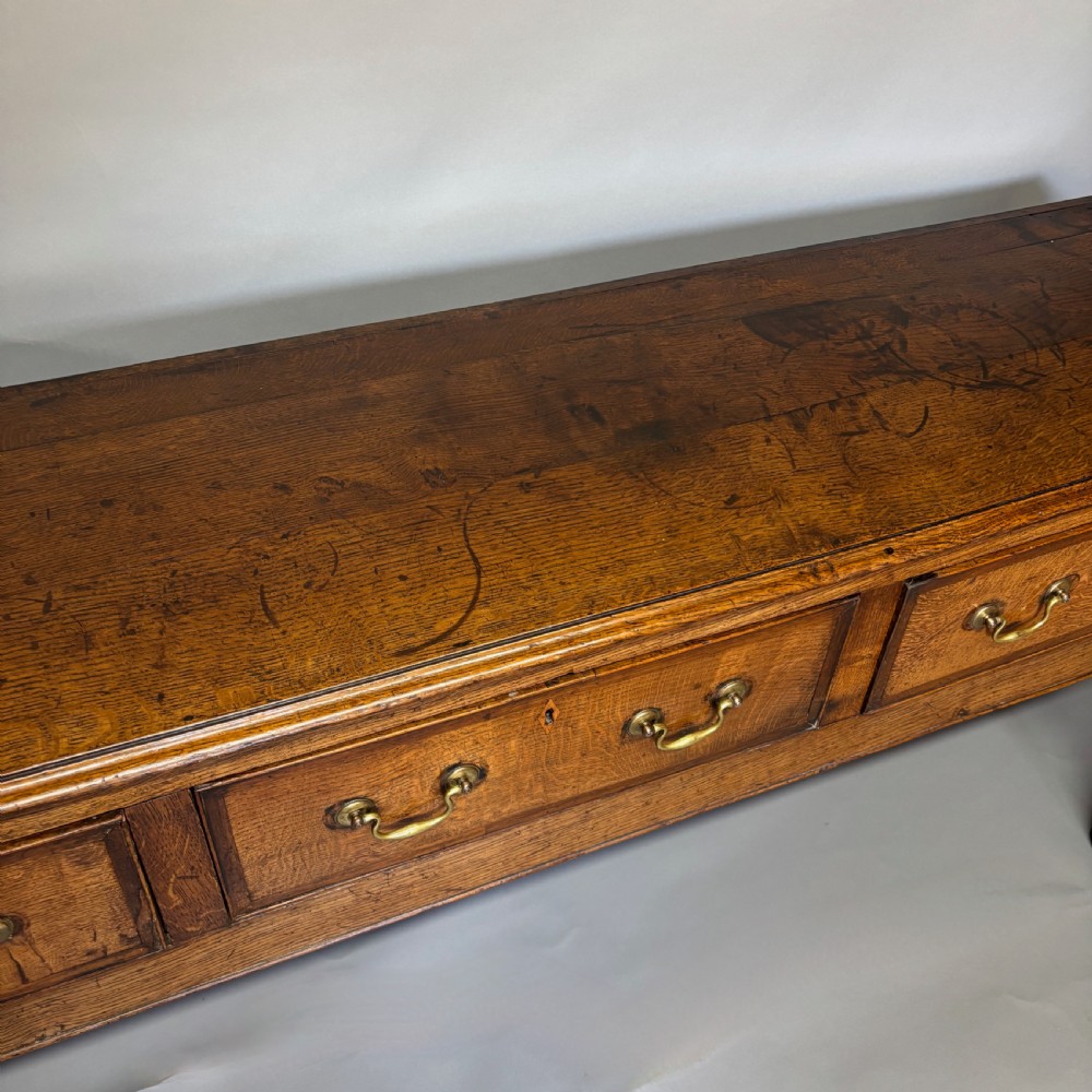 A George III period oak dresser base featuring three drawers with brass swan-neck handles and front cabriole legs. View X