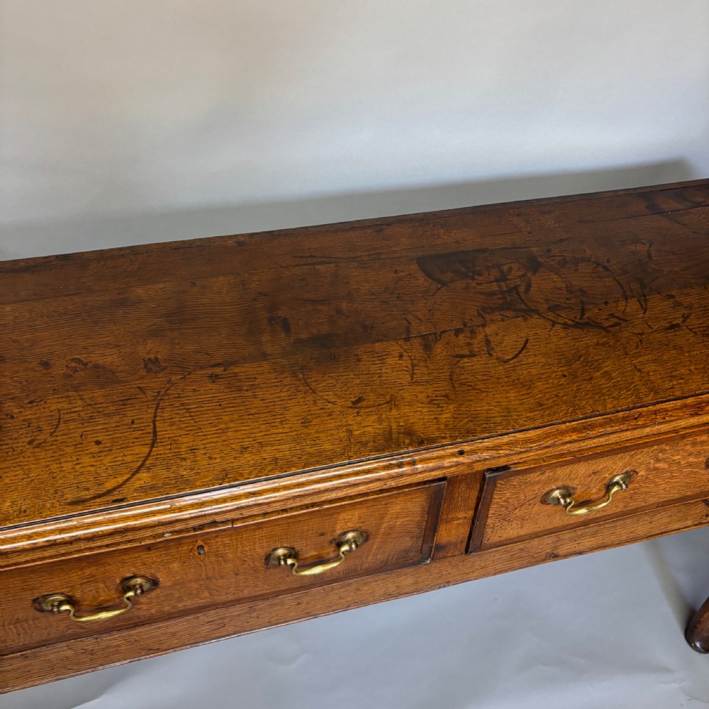 A George III period oak dresser base featuring three drawers with brass swan-neck handles and front cabriole legs. View XIII