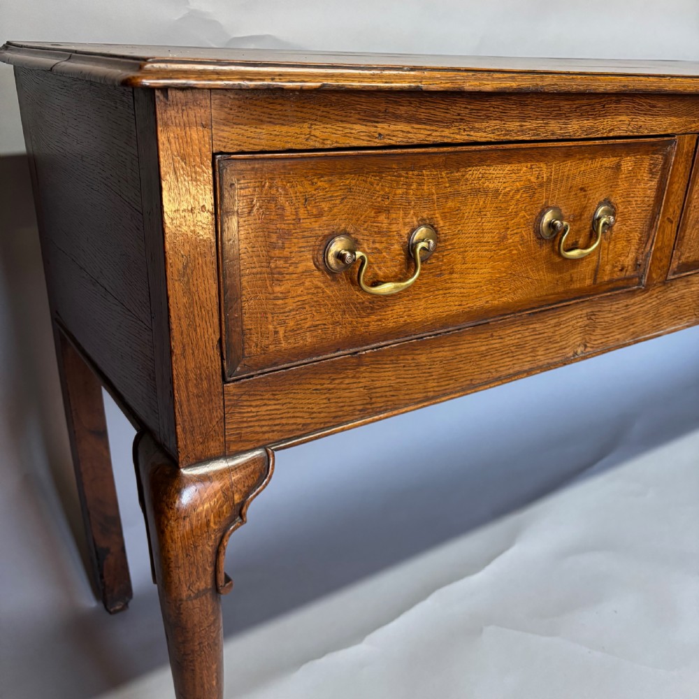A George III period oak dresser base featuring three drawers with brass swan-neck handles and front cabriole legs. View XX