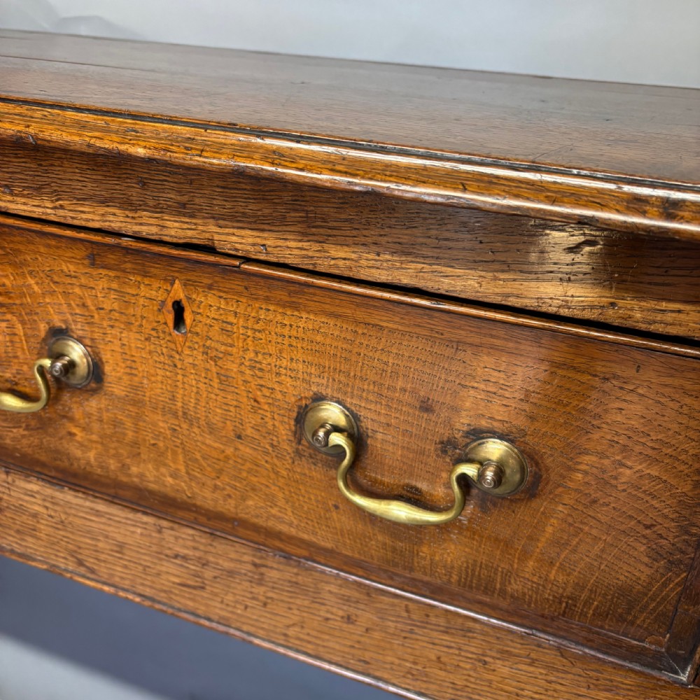 A George III period oak dresser base featuring three drawers with brass swan-neck handles and front cabriole legs. View XXVI