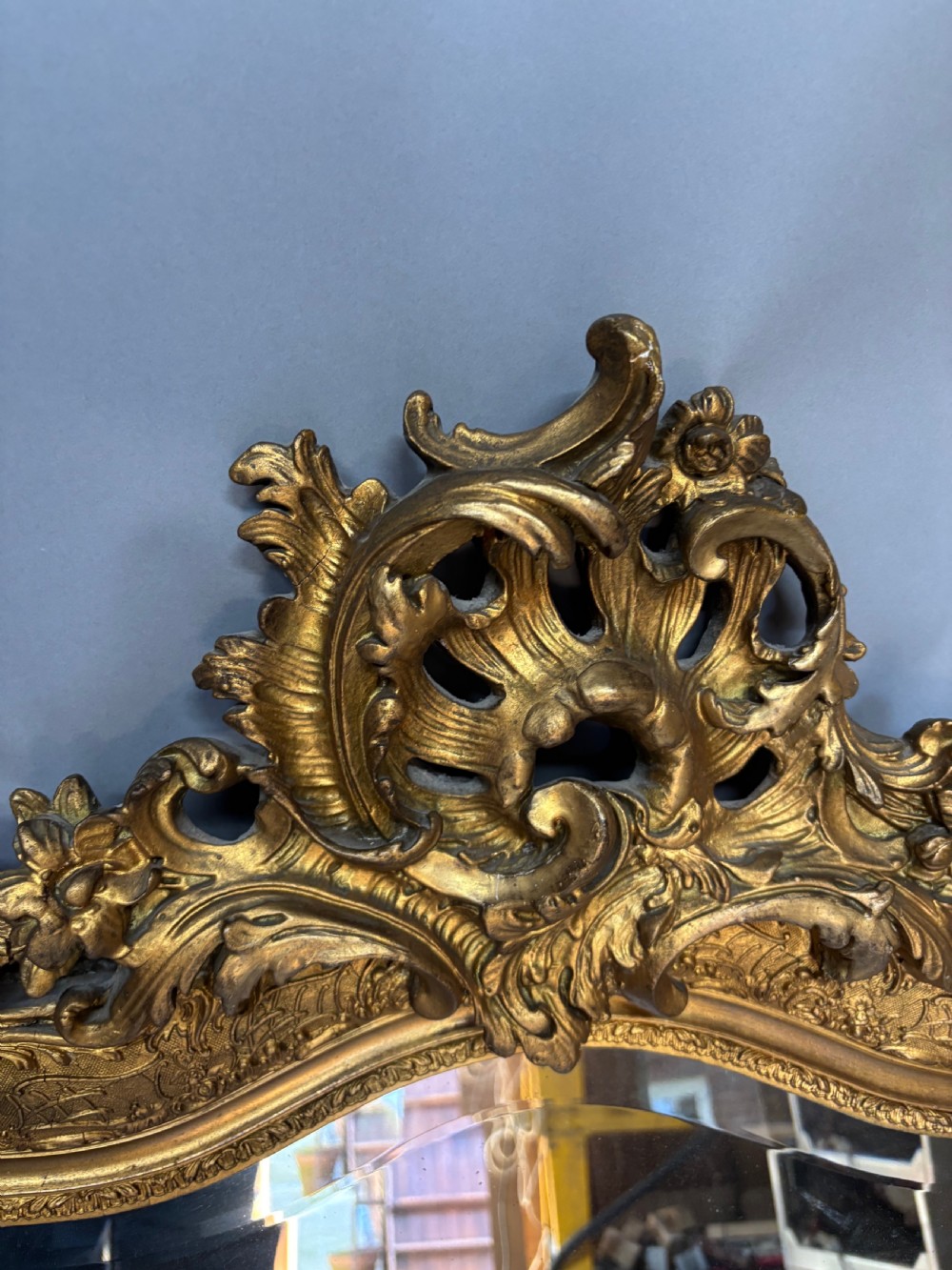 A 19th-century French giltwood wall mirror featuring an intricate floral cresting, molded frame, and carved scroll corner accents. View III