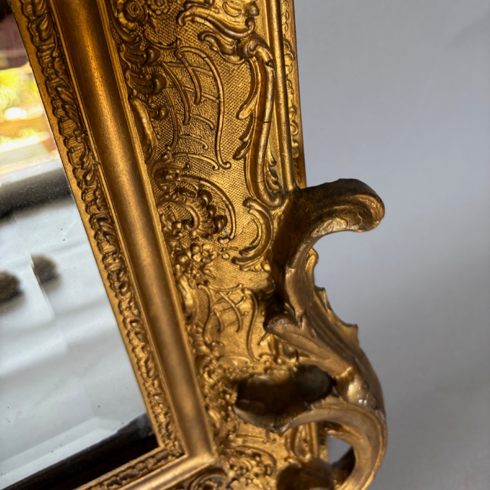 A 19th-century French giltwood wall mirror featuring an intricate floral cresting, molded frame, and carved scroll corner accents. View IV