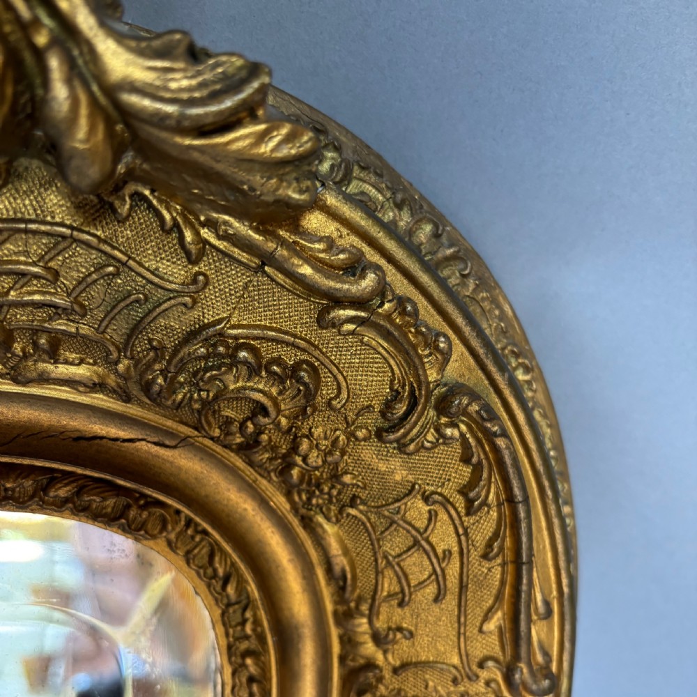 A 19th-century French giltwood wall mirror featuring an intricate floral cresting, molded frame, and carved scroll corner accents. View VII