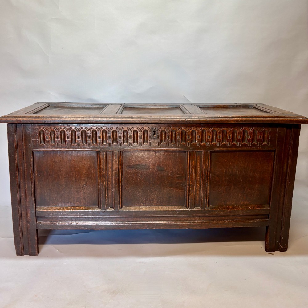 An eighteenth-century dark oak coffer with an arcaded carved top frieze, three lower plain panels, and a panelled hinged top.