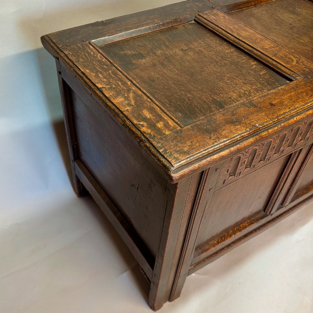 An eighteenth-century dark oak coffer with an arcaded carved top frieze, three lower plain panels, and a panelled hinged top. View II