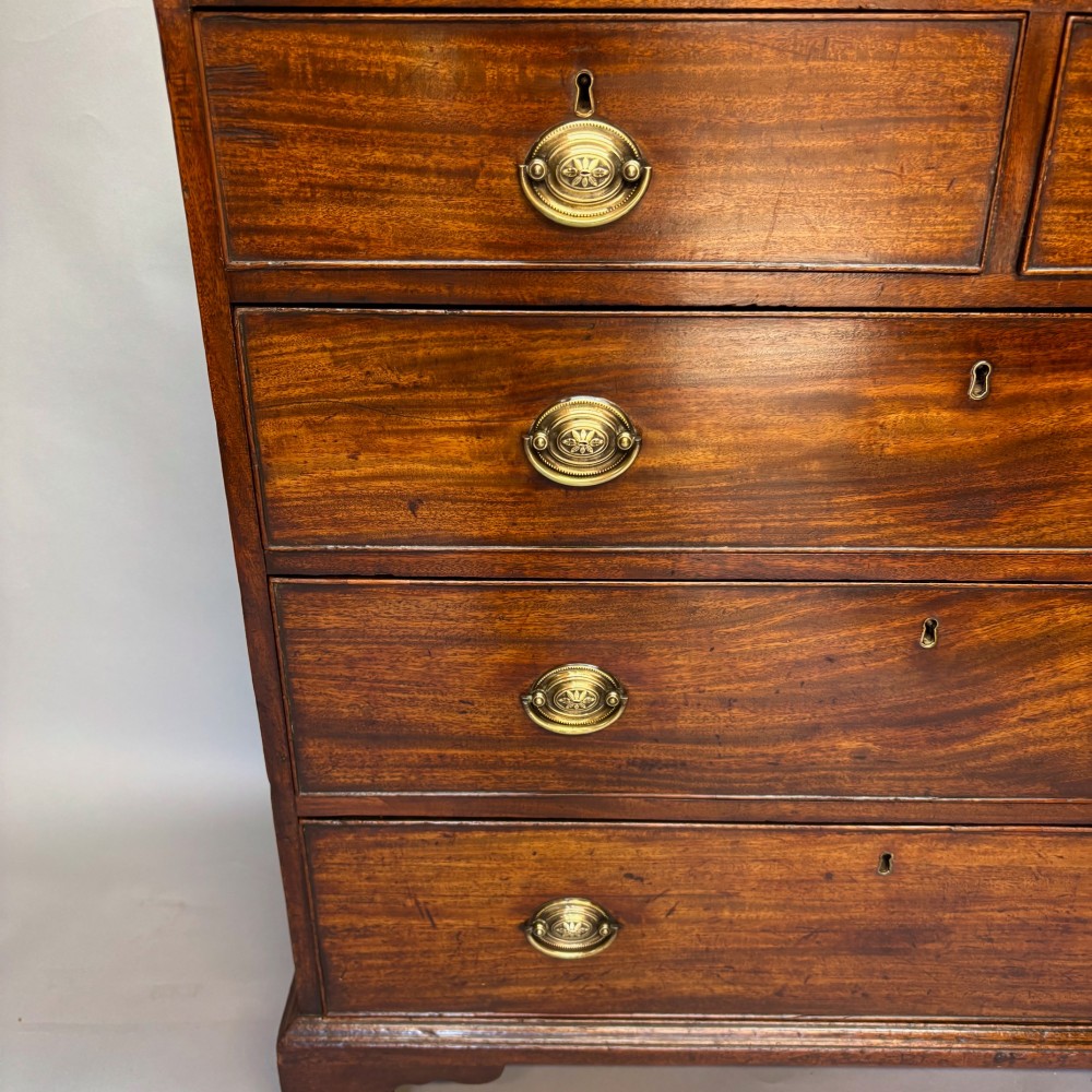 A Georgian George III mahogany chest of drawers featuring two short drawers above three long drawers with oval brass handles and bracket feet. View II