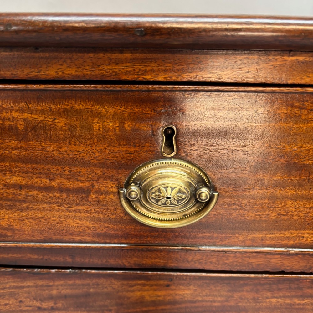A Georgian George III mahogany chest of drawers featuring two short drawers above three long drawers with oval brass handles and bracket feet. View III
