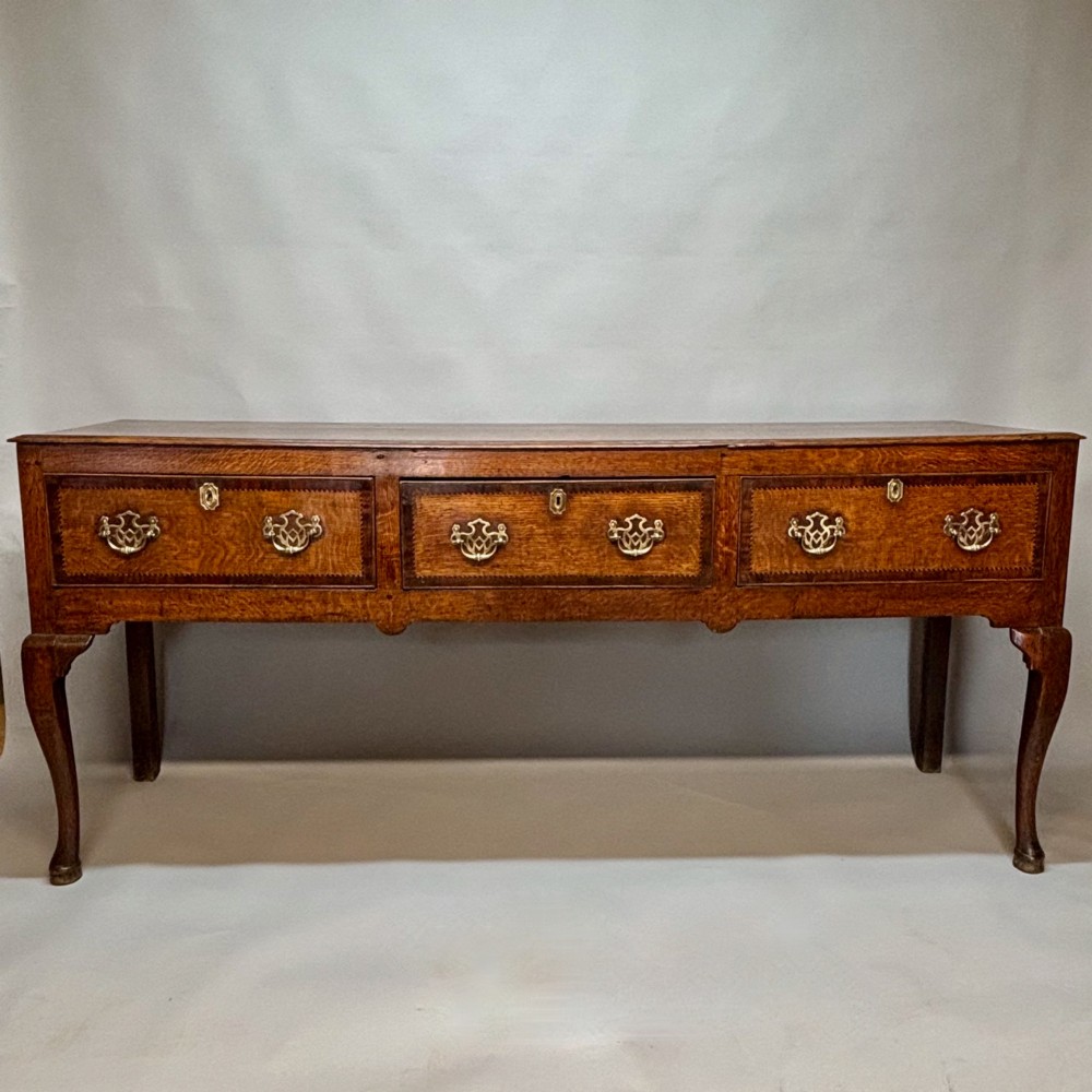 An eighteenth-century oak low dresser featuring three crossbanded drawers with brass swan-neck handles, elevated on four cabriole legs.