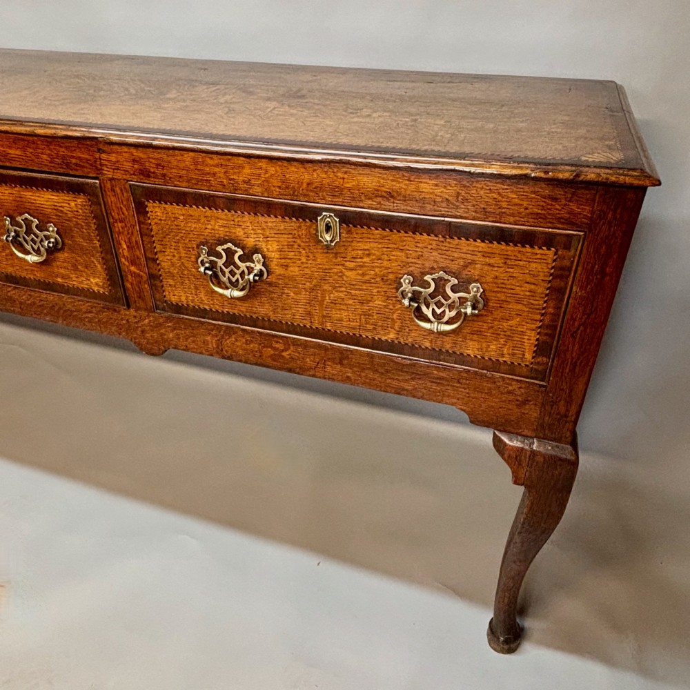 An eighteenth-century oak low dresser featuring three crossbanded drawers with brass swan-neck handles, elevated on four cabriole legs. View II