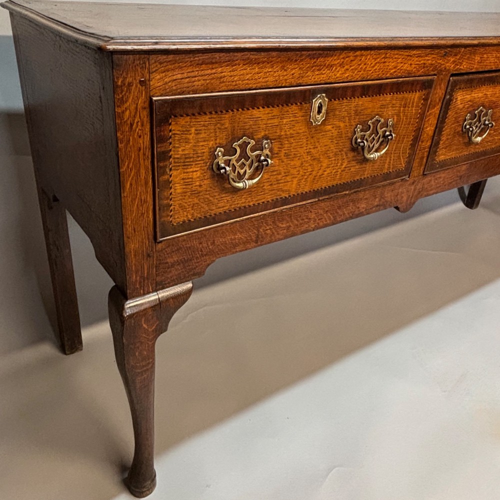 An eighteenth-century oak low dresser featuring three crossbanded drawers with brass swan-neck handles, elevated on four cabriole legs. View III