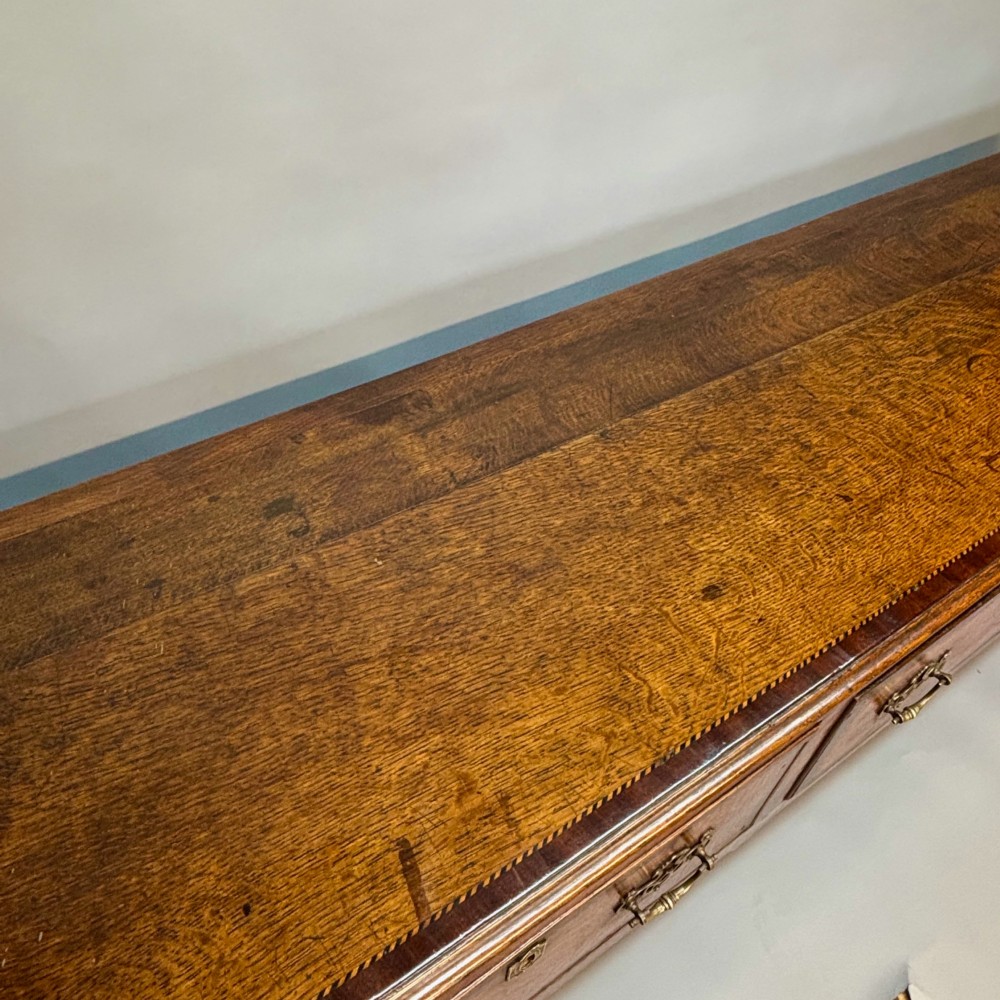 An eighteenth-century oak low dresser featuring three crossbanded drawers with brass swan-neck handles, elevated on four cabriole legs. View IV