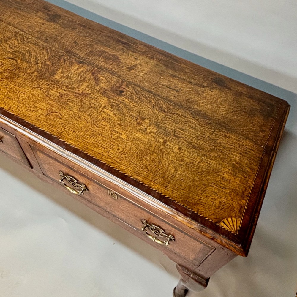An eighteenth-century oak low dresser featuring three crossbanded drawers with brass swan-neck handles, elevated on four cabriole legs. View V