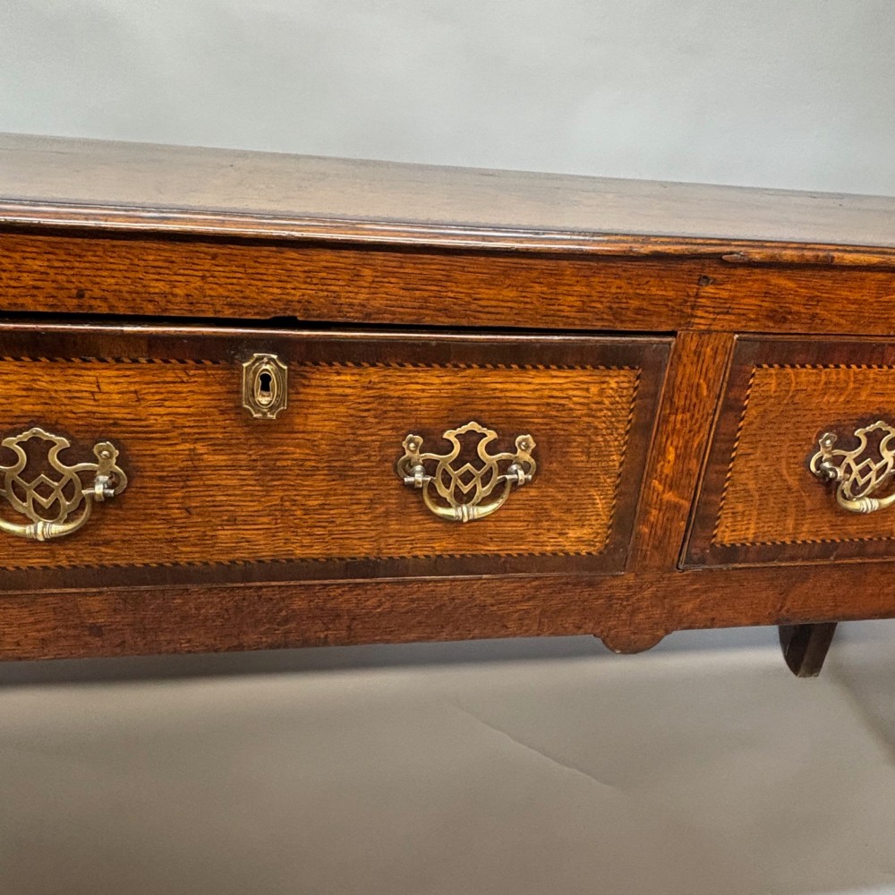 An eighteenth-century oak low dresser featuring three crossbanded drawers with brass swan-neck handles, elevated on four cabriole legs. View VI