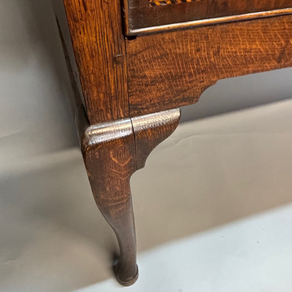 An eighteenth-century oak low dresser featuring three crossbanded drawers with brass swan-neck handles, elevated on four cabriole legs. View XV