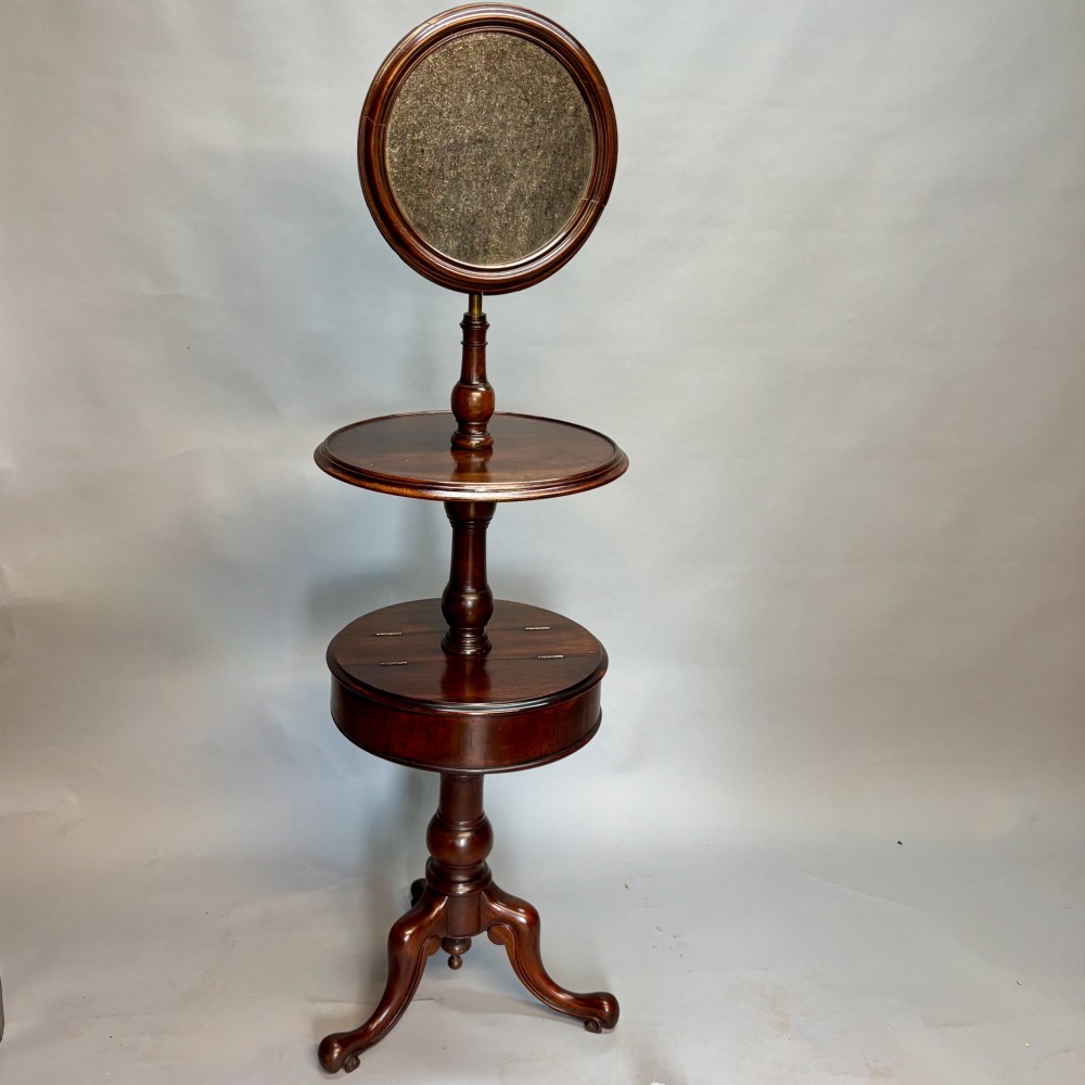 A Victorian dark mahogany shaving stand featuring an adjustable circular mirror, a round tier, a hinged compartment, turned support stem, and tripod cabriole legs.