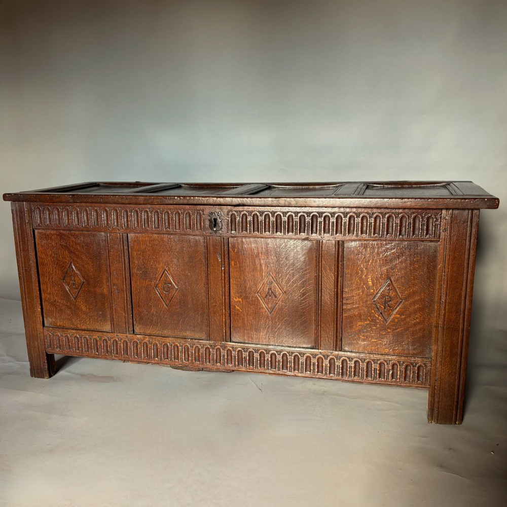 A seventeenth-century dark oak coffer featuring four carved panelled sections with diamond lozenges and decorative carved borders.