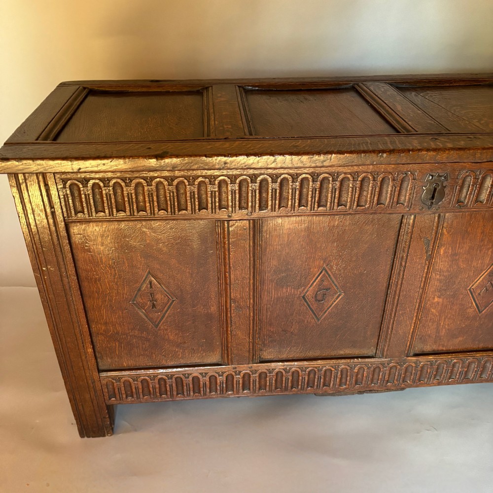 A seventeenth-century dark oak coffer featuring four carved panelled sections with diamond lozenges and decorative carved borders. View II
