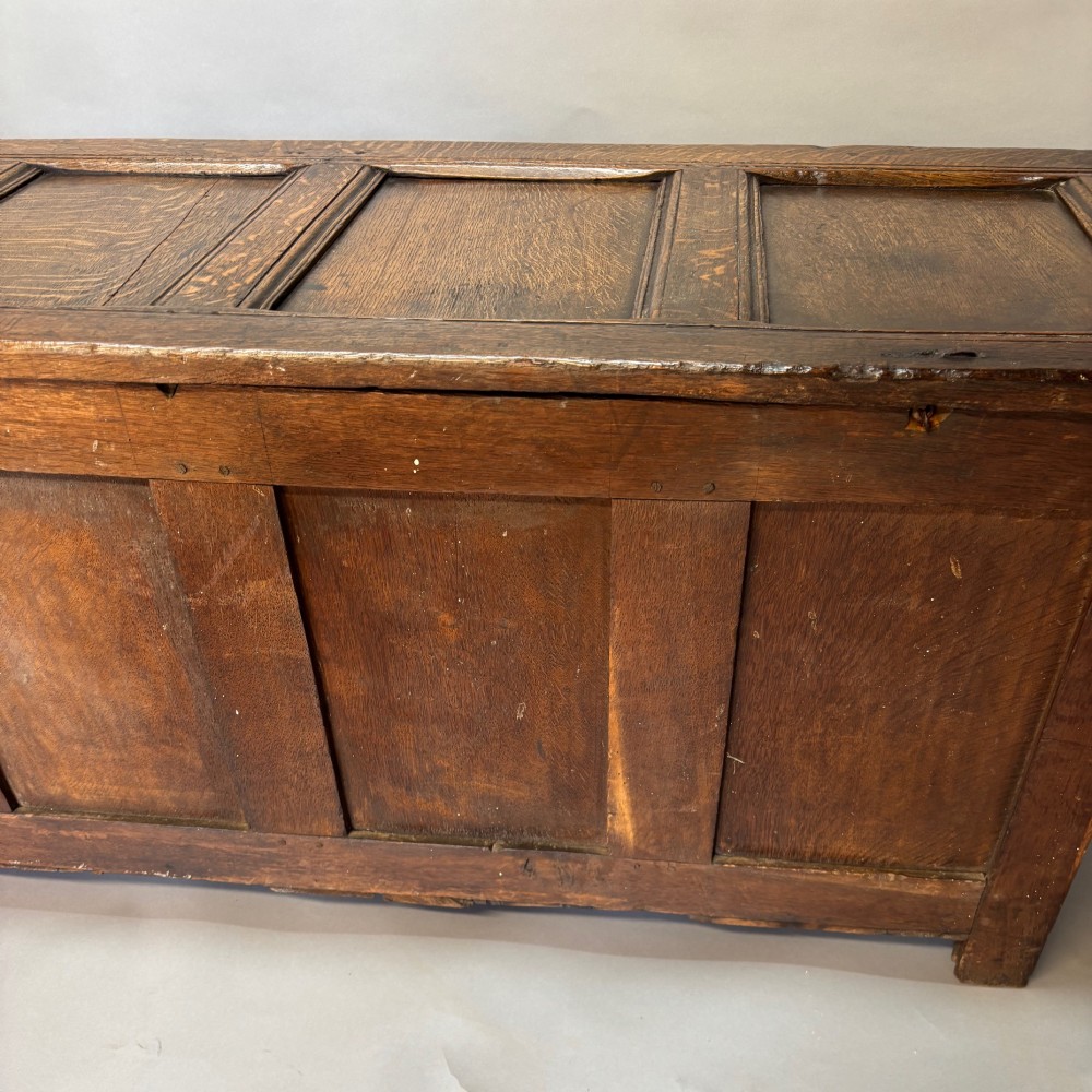 A seventeenth-century dark oak coffer featuring four carved panelled sections with diamond lozenges and decorative carved borders. View IV