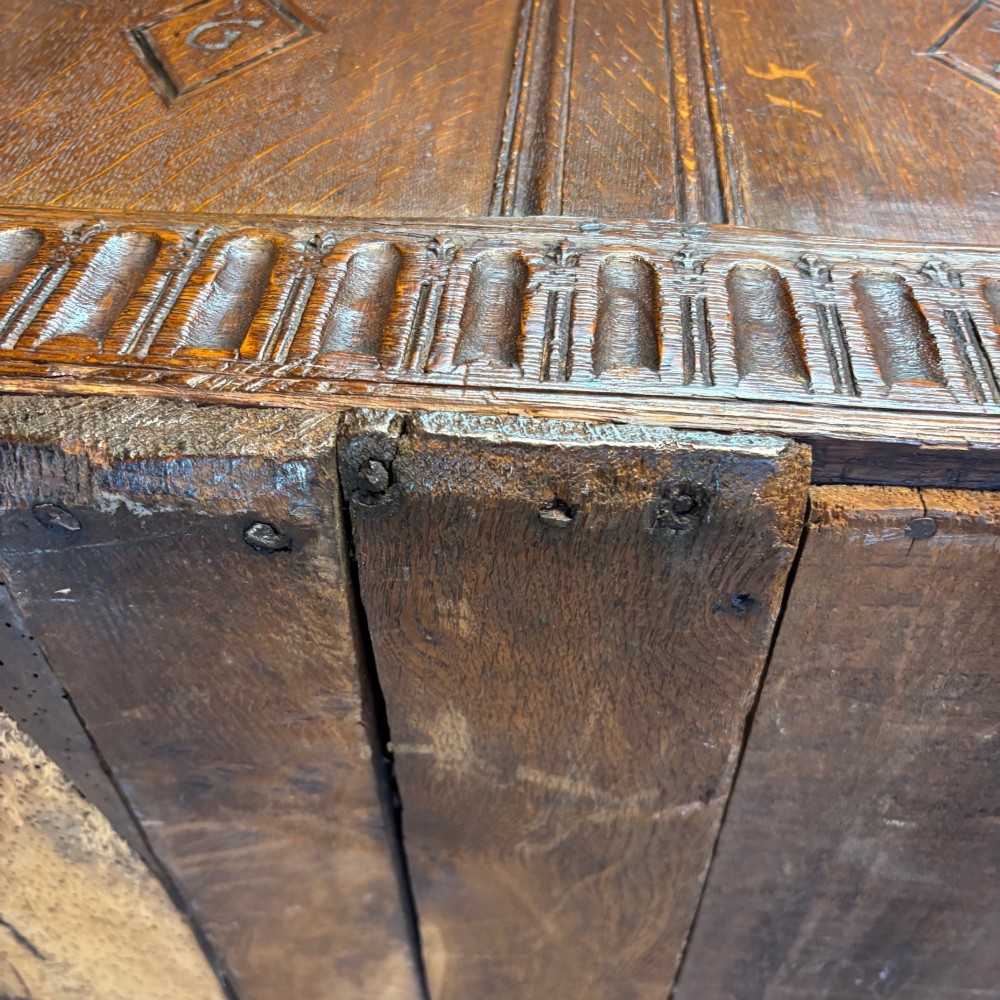 A seventeenth-century dark oak coffer featuring four carved panelled sections with diamond lozenges and decorative carved borders. View V