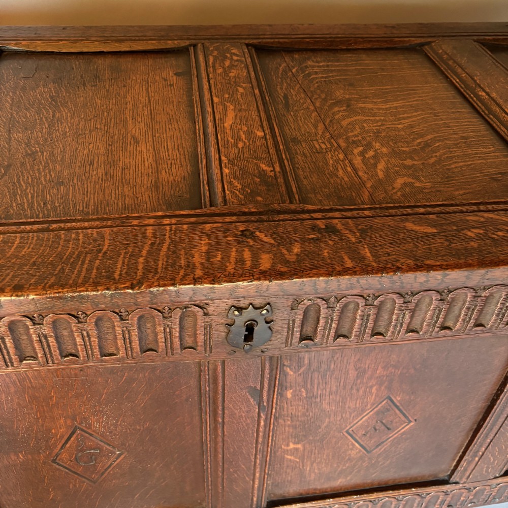 A seventeenth-century dark oak coffer featuring four carved panelled sections with diamond lozenges and decorative carved borders. View X