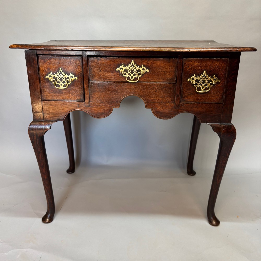 An 18th-century George II oak lowboy featuring three drawers with pierced brass handles, a shaped apron, and four cabriole legs with pad feet.