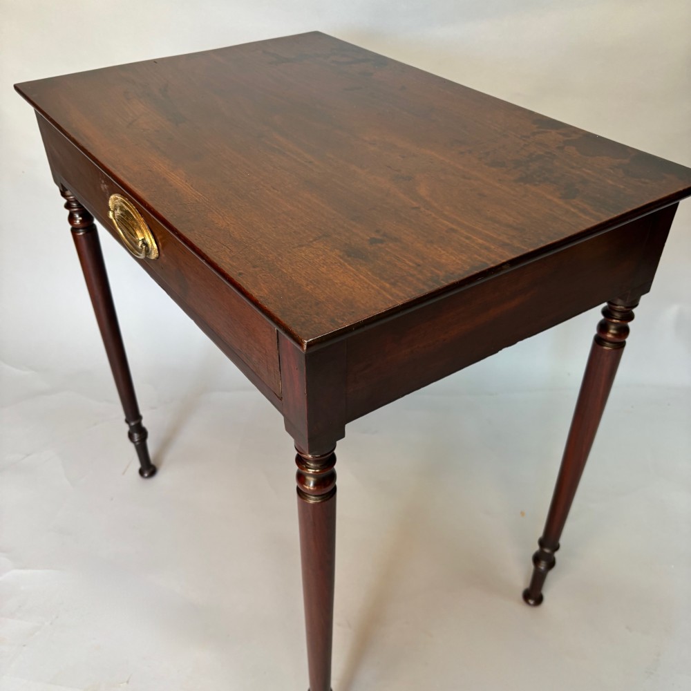 A George III mahogany side table featuring a single drawer with an oval brass handle and slender turned legs. View II