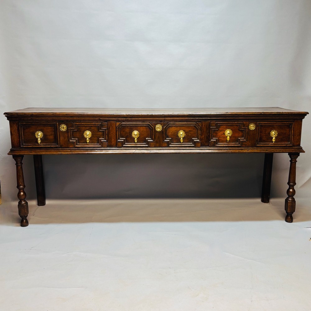 A late 17th-century dark oak low dresser featuring geometric moulded drawer fronts, brass teardrop handles, and turned front legs.