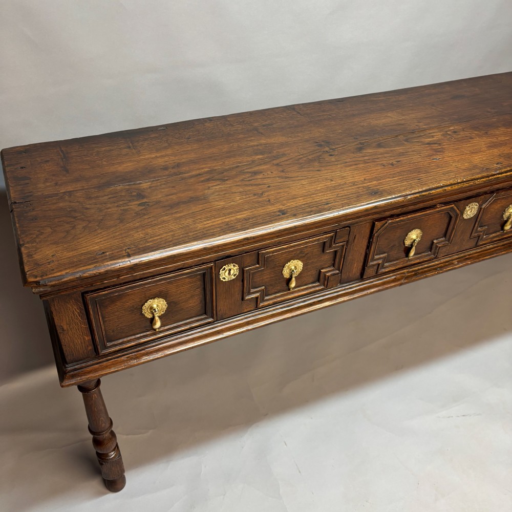 A late 17th-century dark oak low dresser featuring geometric moulded drawer fronts, brass teardrop handles, and turned front legs. View II