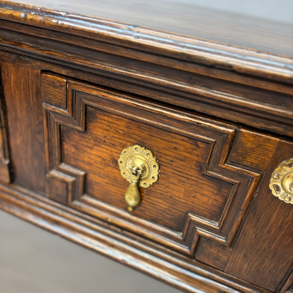 A late 17th-century dark oak low dresser featuring geometric moulded drawer fronts, brass teardrop handles, and turned front legs. View III