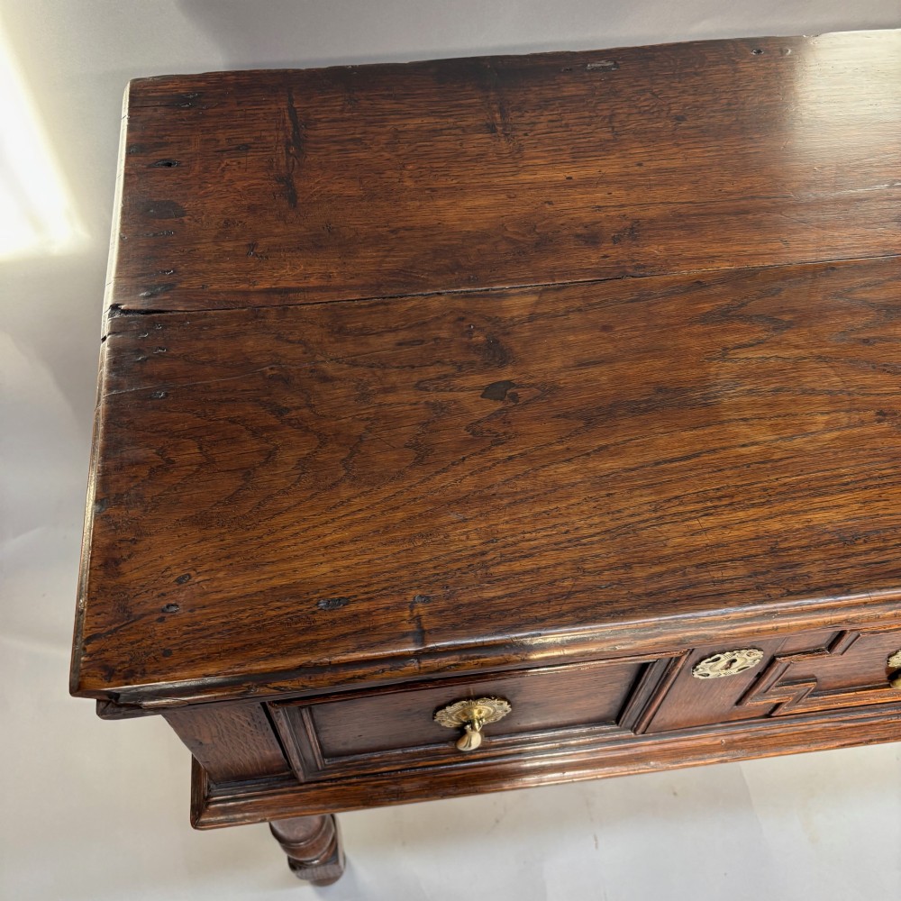 A late 17th-century dark oak low dresser featuring geometric moulded drawer fronts, brass teardrop handles, and turned front legs. View IV