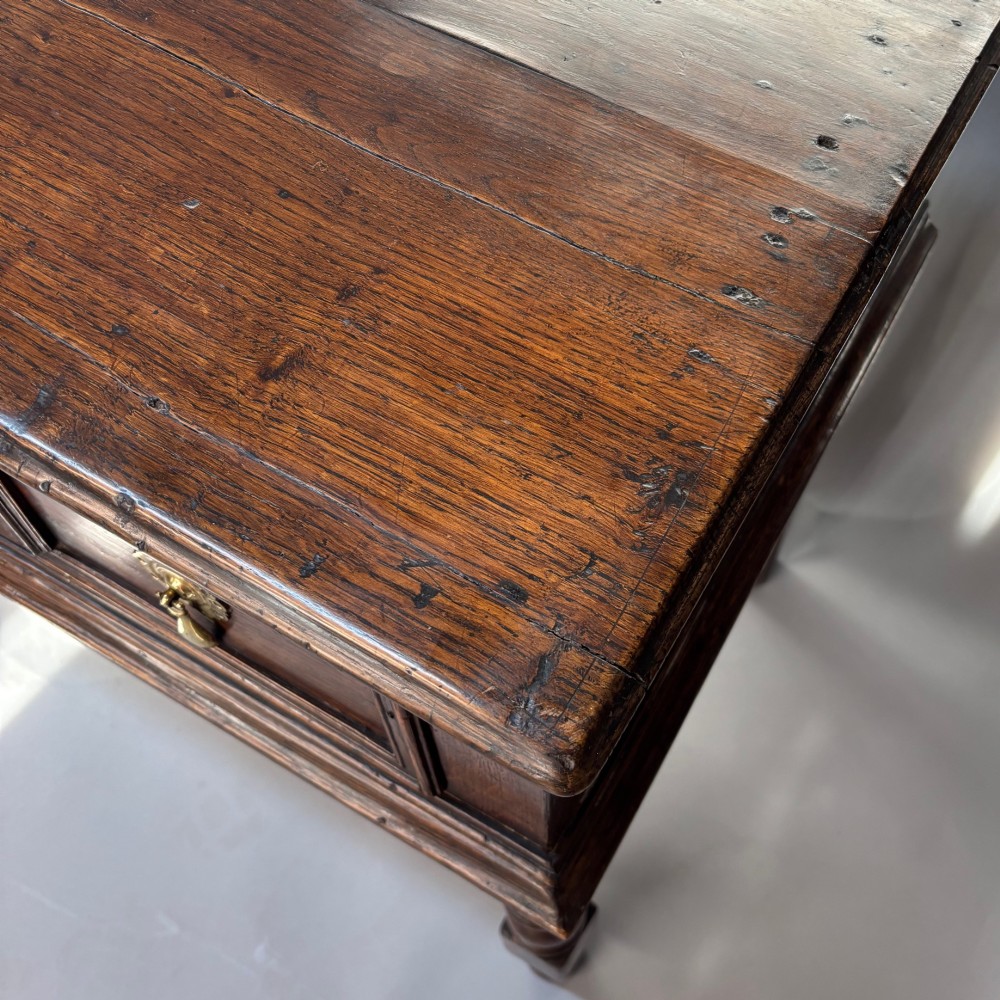 A late 17th-century dark oak low dresser featuring geometric moulded drawer fronts, brass teardrop handles, and turned front legs. View V