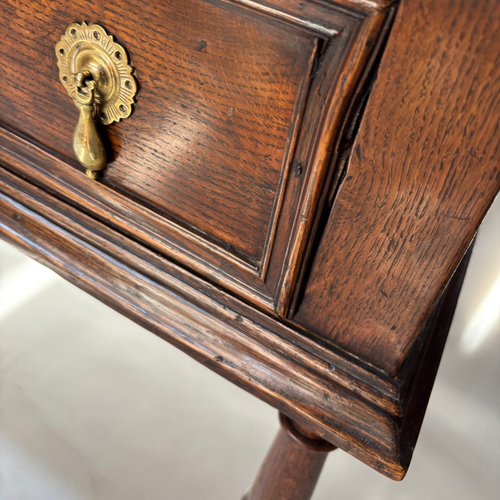 A late 17th-century dark oak low dresser featuring geometric moulded drawer fronts, brass teardrop handles, and turned front legs. View VI