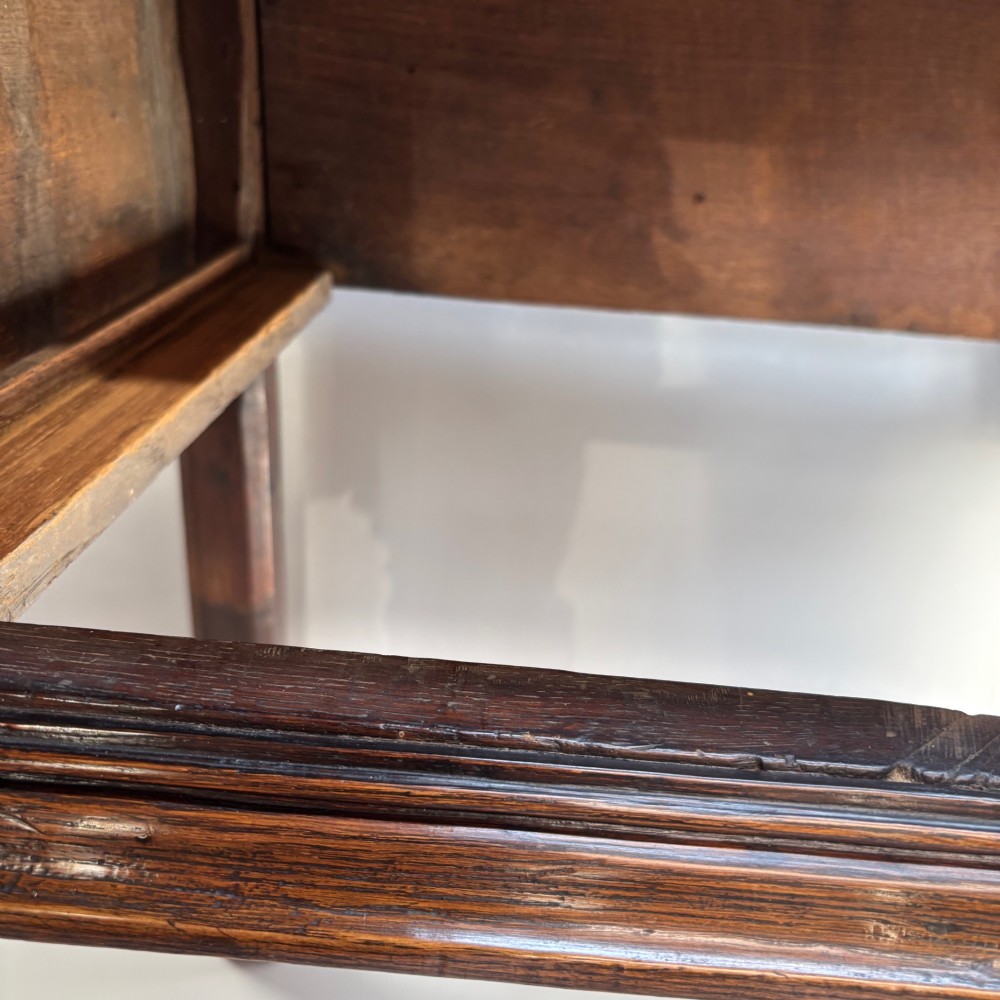 A late 17th-century dark oak low dresser featuring geometric moulded drawer fronts, brass teardrop handles, and turned front legs. View X