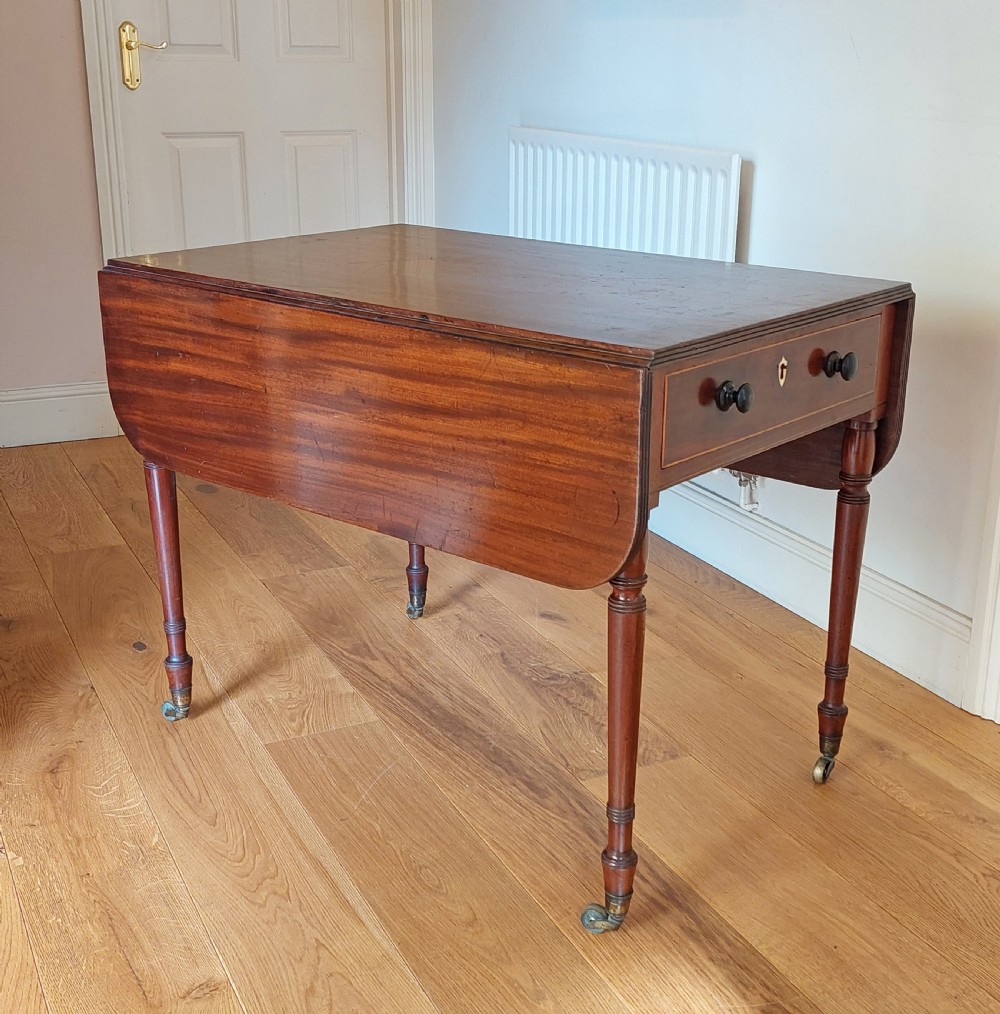 A Regency mahogany Pembroke table featuring drop flaps, a drawer with turned wood knobs, and reeded turned legs on brass castors.