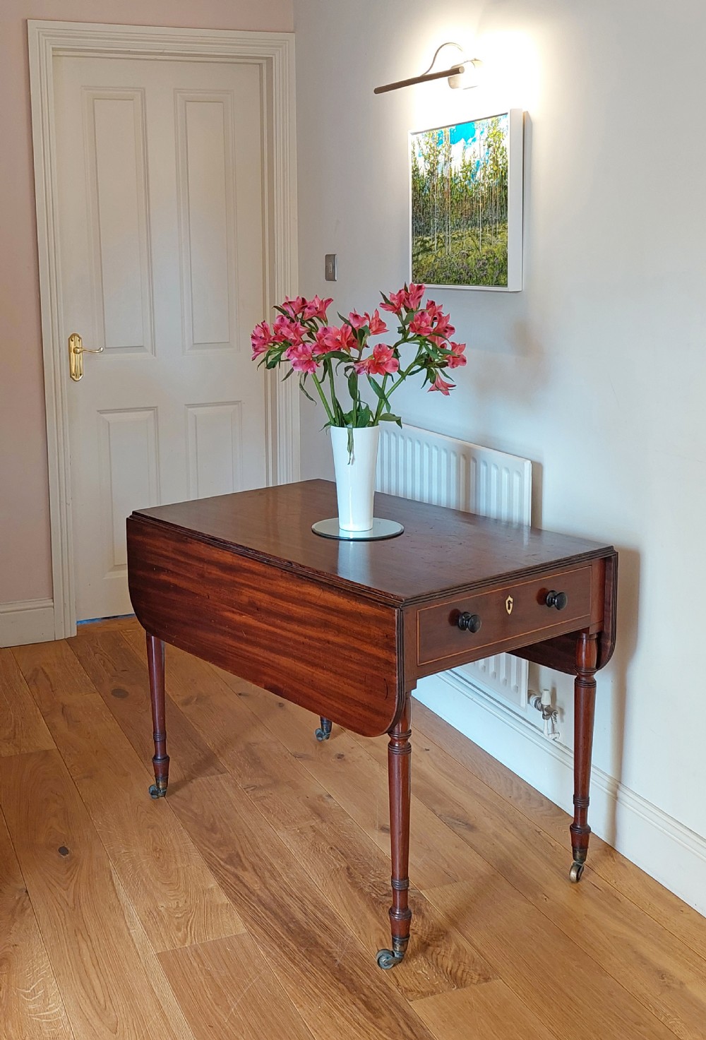 A Regency mahogany Pembroke table featuring drop flaps, a drawer with turned wood knobs, and reeded turned legs on brass castors. View II
