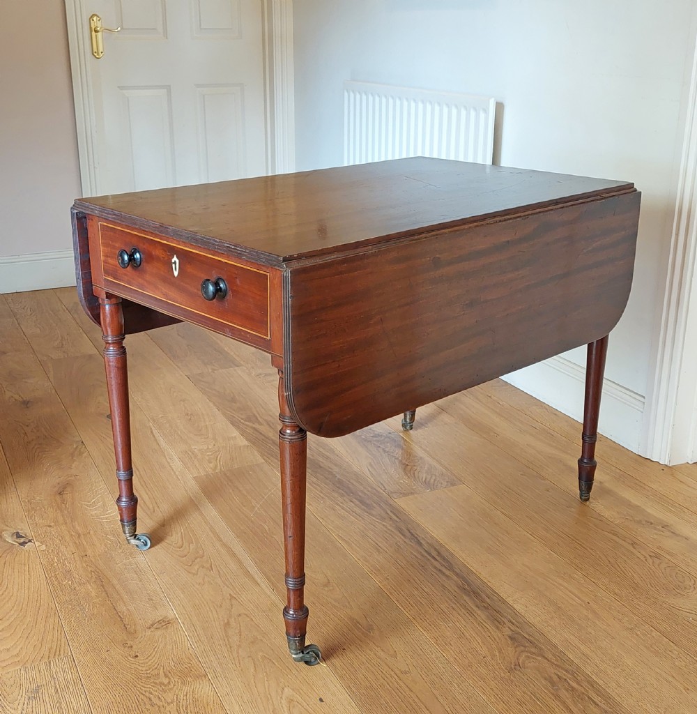 A Regency mahogany Pembroke table featuring drop flaps, a drawer with turned wood knobs, and reeded turned legs on brass castors. View III
