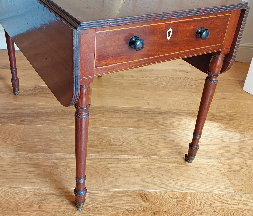 A Regency mahogany Pembroke table featuring drop flaps, a drawer with turned wood knobs, and reeded turned legs on brass castors. View IV