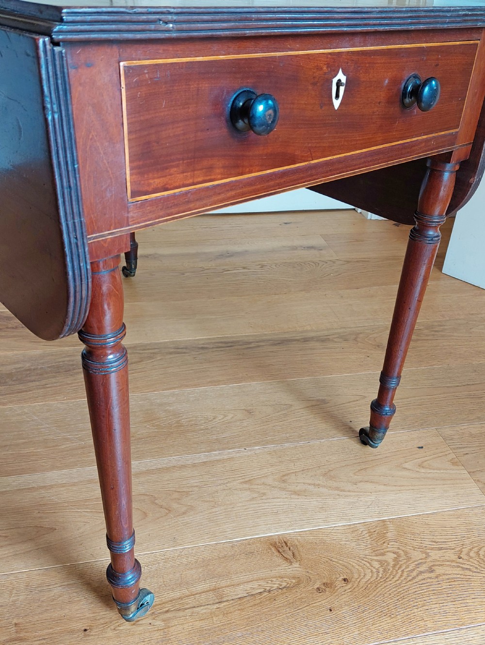 A Regency mahogany Pembroke table featuring drop flaps, a drawer with turned wood knobs, and reeded turned legs on brass castors. View V