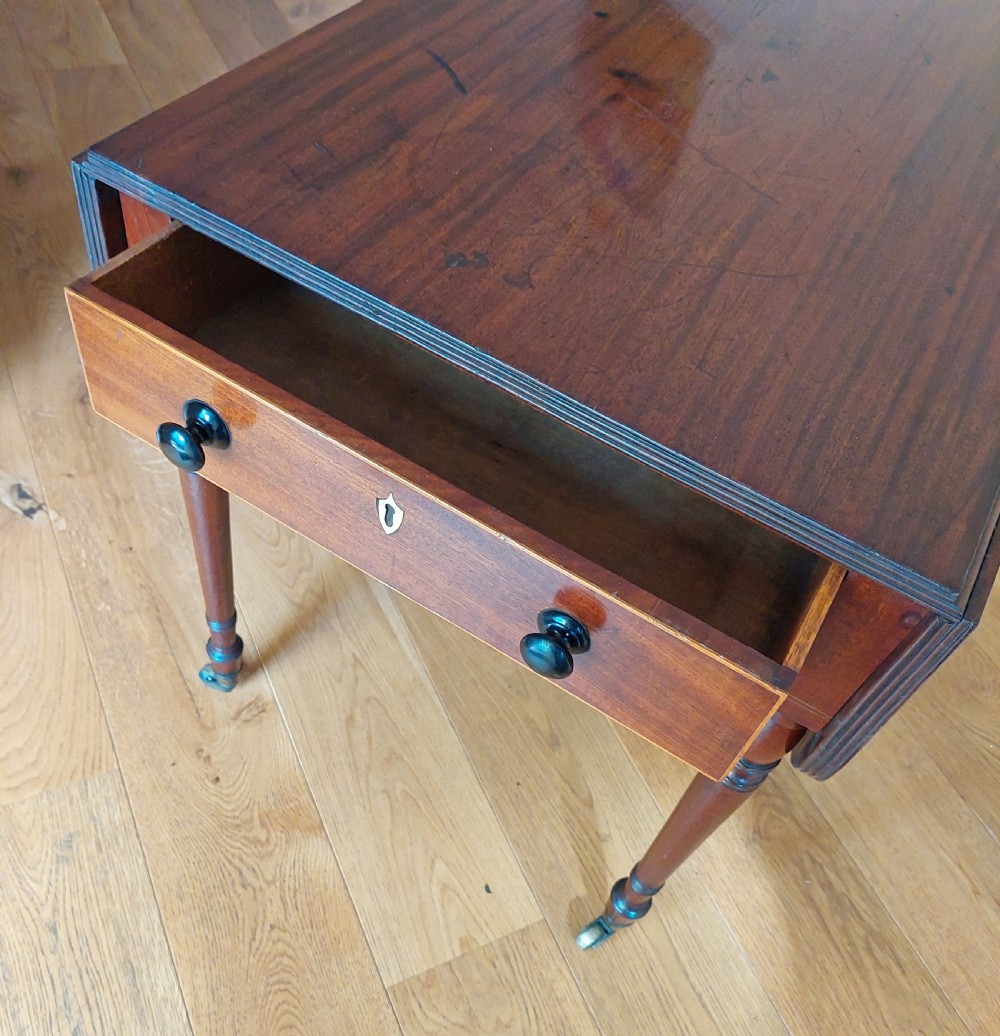A Regency mahogany Pembroke table featuring drop flaps, a drawer with turned wood knobs, and reeded turned legs on brass castors. View IX