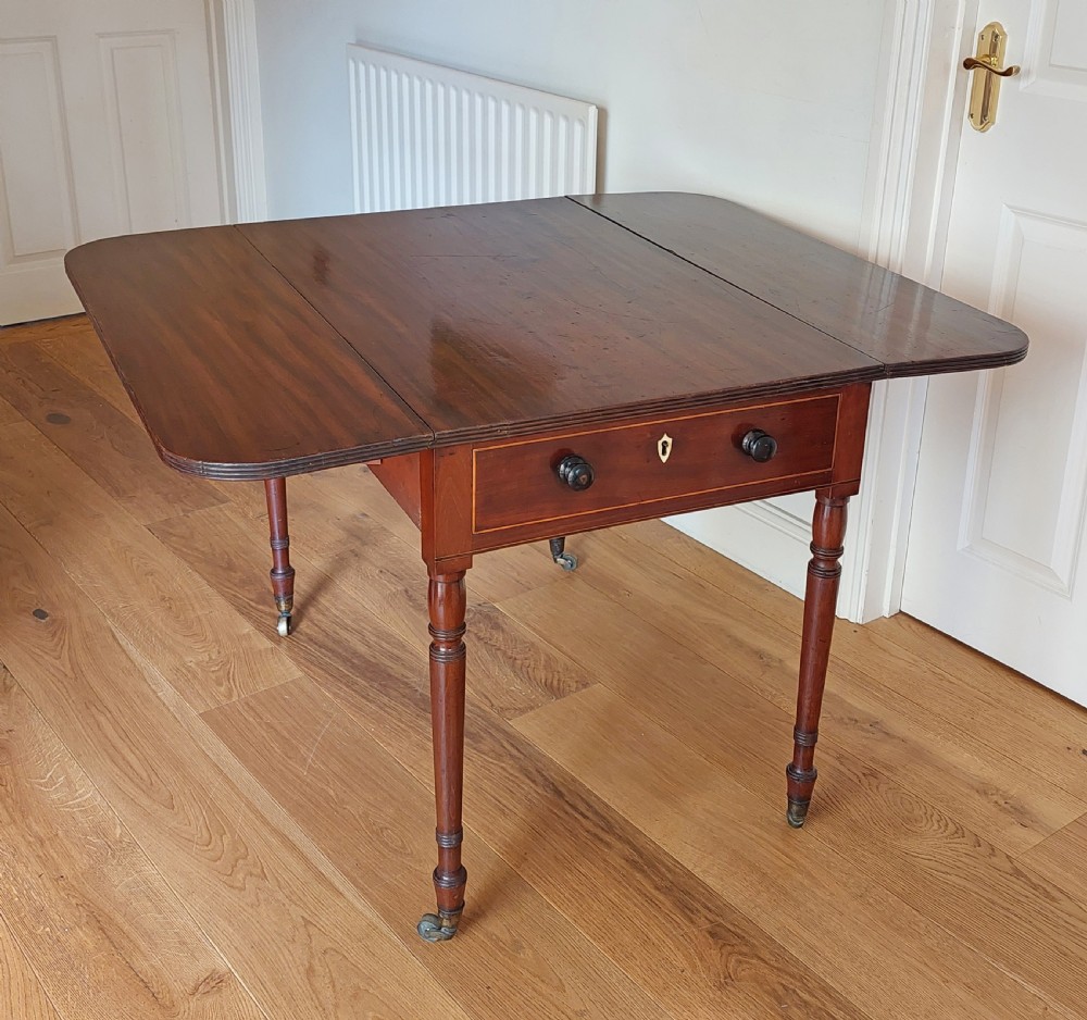 A Regency mahogany Pembroke table featuring drop flaps, a drawer with turned wood knobs, and reeded turned legs on brass castors. View X