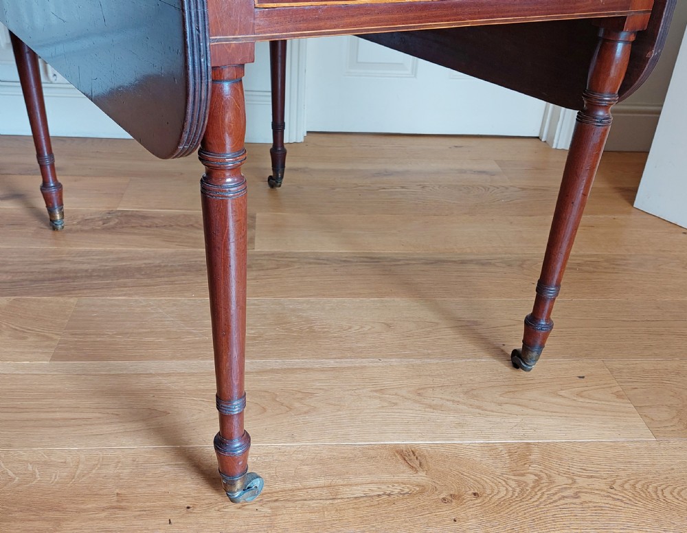 A Regency mahogany Pembroke table featuring drop flaps, a drawer with turned wood knobs, and reeded turned legs on brass castors. View XII