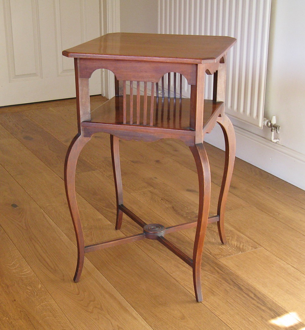 An early twentieth-century mahogany two-tier occasional table featuring slender cabriole legs, vertical spindles on the lower shelf, and a central circular motif on the X-stretcher.