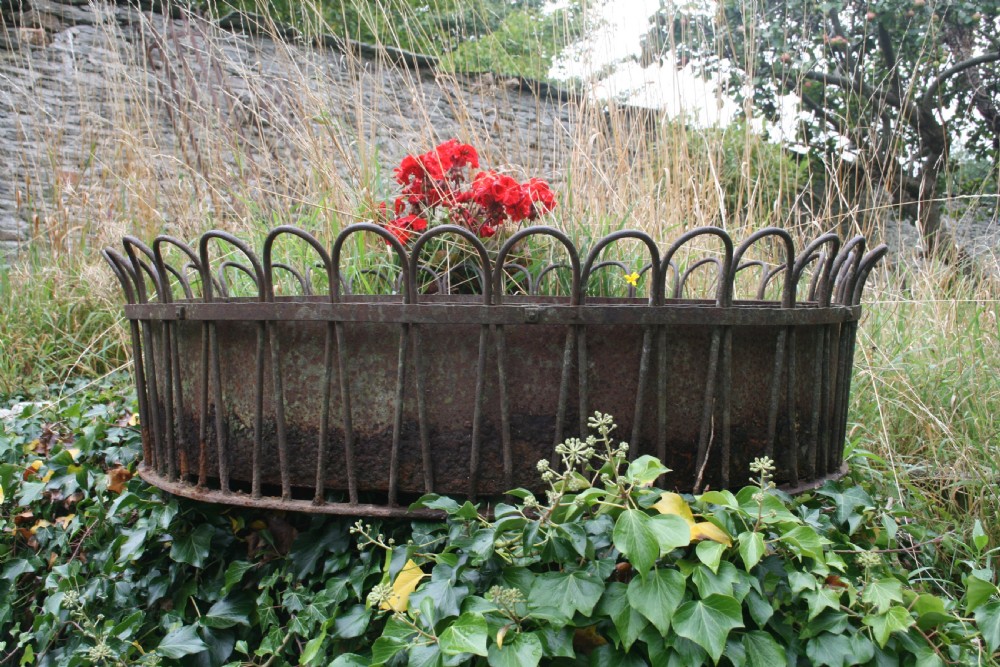 A large circular wrought iron garden planter with an outer frame of vertical bars forming looped arches over an oxidised metal interior lining.