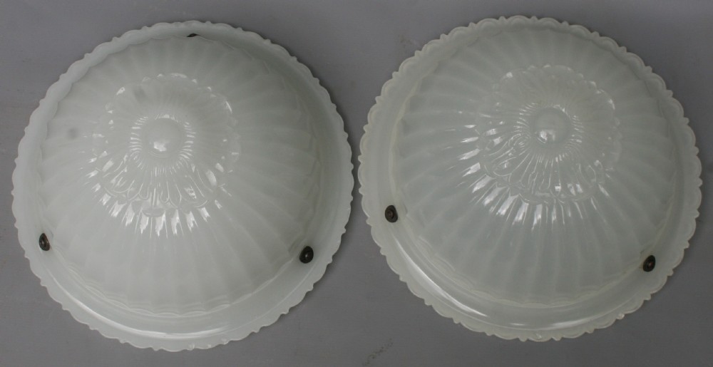 A pair of circular, translucent white opaline glass ceiling light shades featuring moulded fluted patterns and scalloped rims.